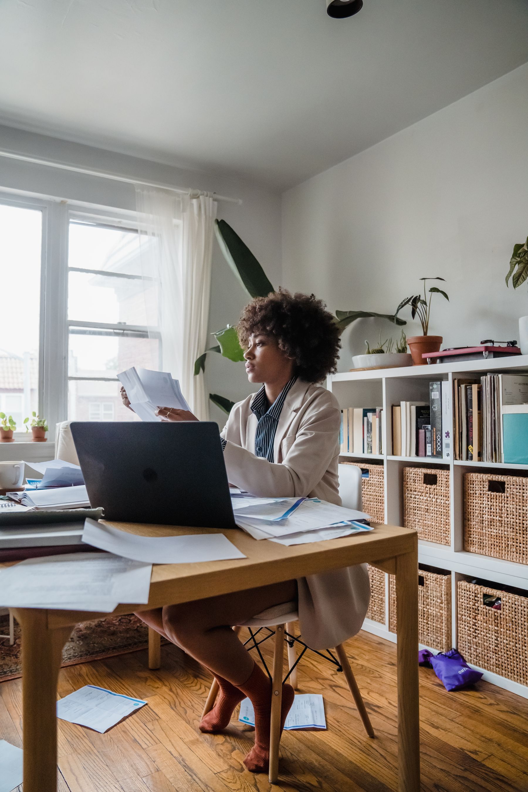 A woman reviews paperwork at a table in a bright home office.
